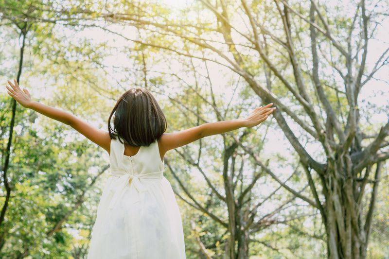 Girl standing joyfully under green trees